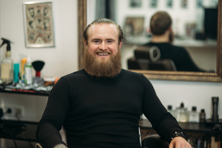 handsome young bearded guy sitting in an armchair in a beauty salonの写真素材