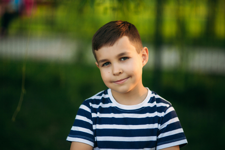 A little boy in a striped T-shirt standing in front of green background. Smiling and looking to the photographerの写真素材