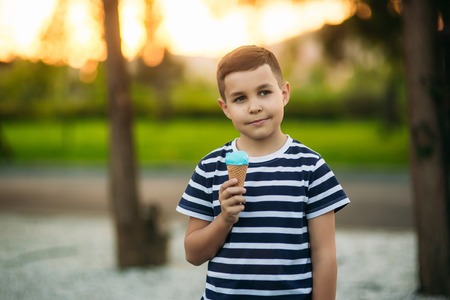 A little boy in a striped T-shirt is eating blue ice cream.Spring, sunny weatherの写真素材