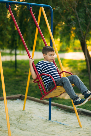 A little boy in a striped T-shirt is playing on the playground, Swing on a swing.の写真素材