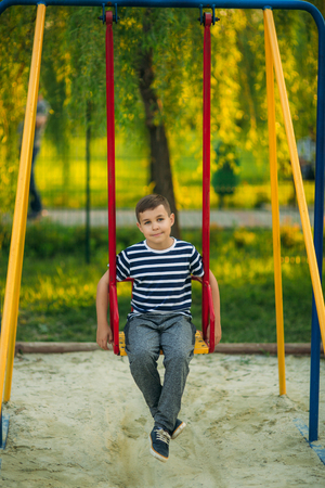 A little boy in a striped T-shirt is playing on the playground, Swing on a swing.の写真素材