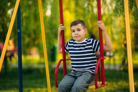 A little boy in a striped T-shirt is playing on the playground, Swing on a swing.の写真素材