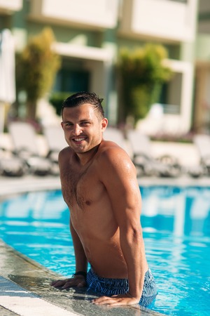 Close up portrait of attractive young man resting on edge of swimming poolの写真素材