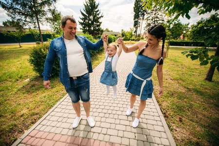 Happy joyful young family father, mother and little daughter having fun outdoors, playing together in summer park, countryside. Mom, Dad and kid laughing and hugging, enjoying nature outsideの写真素材