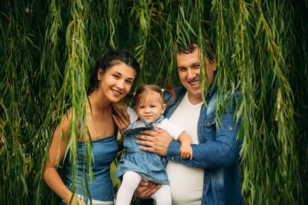 Happy joyful young family father, mother and little daughter having fun outdoors, playing together in summer park, countryside. Mom, Dad and kid laughing and hugging, enjoying nature outsideの写真素材