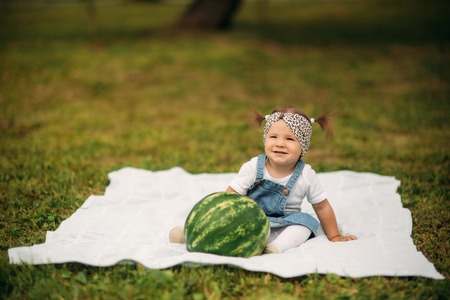 Little girl sitting in a park on plaid and eating a watermelonの写真素材