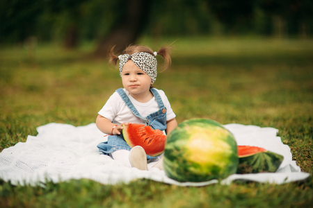 Little girl sitting in a park on plaid and eating a watermelonの写真素材