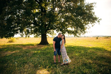 Handsome guy and an attractive girl hug each other near a large green tree. Love storyの写真素材