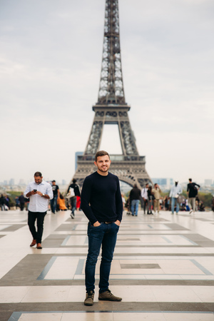 Handsome man wearing a dark blue pullover is standing on the background of the Eiffel Towerの写真素材