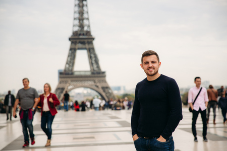Cheerful man in dark blue pullover is standing on the background of the Eiffel Towerの写真素材