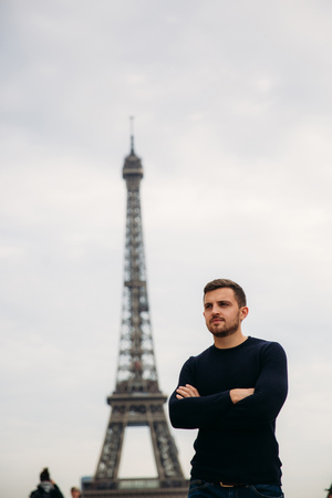 Handsome man wearing a dark blue pullover is standing on the background of the Eiffel Towerの写真素材