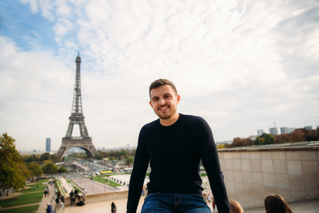 Cheerful man in dark blue pullover is standing on the background of the Eiffel Towerの写真素材