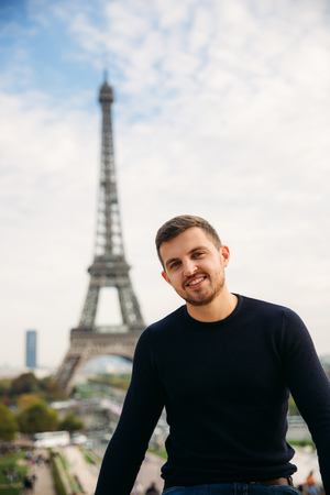 Cheerful man in dark blue pullover is standing on the background of the Eiffel Towerの写真素材