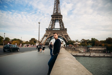 Handsome man in dark pullover is standing on the bridge background of the Eiffel Towerの写真素材