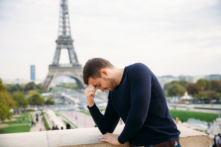Handsome man wearing a dark blue pullover is standing on the background of the Eiffel Towerの写真素材
