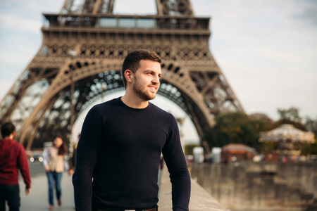Handsome man in dark pullover is standing on the bridge background of the Eiffel Towerの写真素材