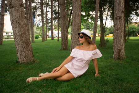 Beautiful girl indress and hat in the park. Green grass and sunny. Background of treesの写真素材