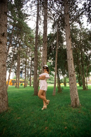 Beautiful girl indress and hat in the park. Green grass and sunny. Background of treesの写真素材