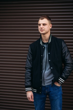 A young guy in a black jacket against a background of dark striped wallの写真素材