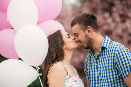 Young happy couple in love outdoors. Handsome man and beautiful woman on a walk in a spring blooming park. They keep helium ballsの写真素材