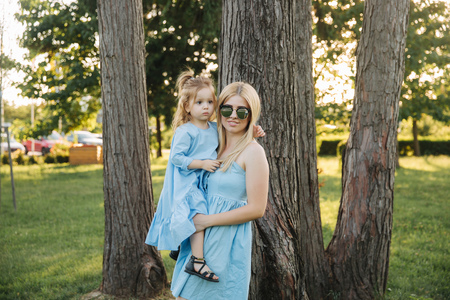 Young beautiful woman with her little cute daughter. Young daughter hugs mother in summer parkの写真素材