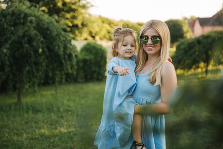 Young beautiful woman with her little cute daughter. Young daughter hugs mother in summer parkの写真素材
