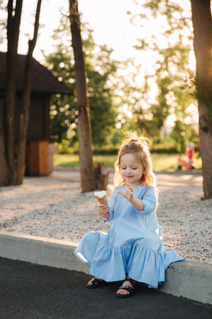 Beautiful little girl in a blue dress eating an ice creamの写真素材