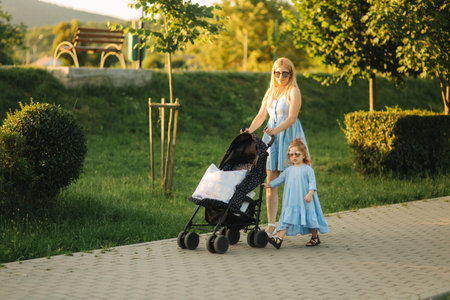 little daughter helps mom push the baby carriage. Happy family