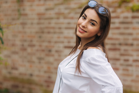 Portrait of happy female in sunglasses. Girl is dressed in a white shirt is standing near a wall overgrown with ivyの写真素材
