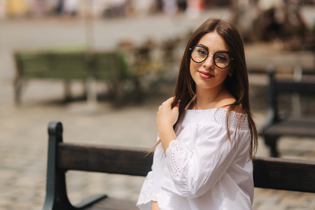 Beautiful girl sits on benth in centre of city. She relaxes and waits for her husbandの写真素材
