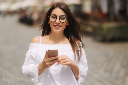 Attractive smiling young female texting on cell phone outdoors in cityの写真素材