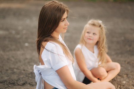 Attractive Mom and blonde hair daughter sits on road near big alley. They smile and look to natuneの写真素材