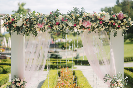Weddind decoration on open air. Floral decor of a beautiful white arch. Beautiful beckground view of treesの写真素材