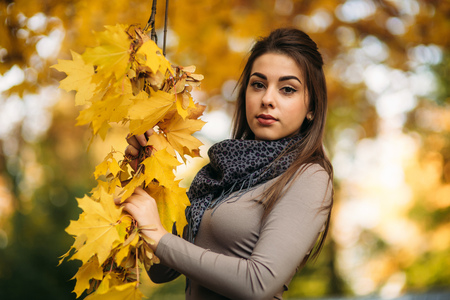 Beautiful autumn woman with autumn leaves on fall nature background. Branch with yellow leavesの写真素材