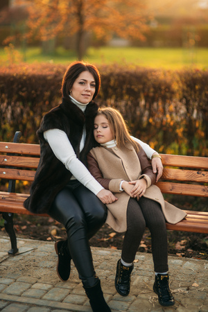 Mother and little daughter is sitting on a bench in the parkの写真素材
