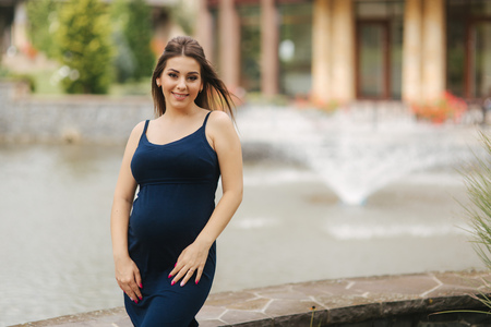 Beautiful young cheerful pregnant woman standing in background of fountainの写真素材