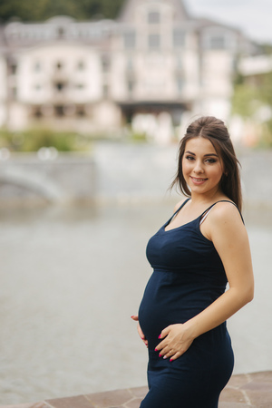 Beautiful young cheerful pregnant woman standing in background of fountainの写真素材