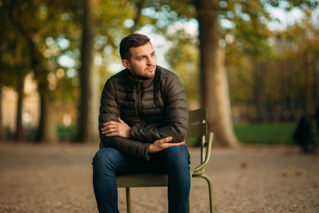 Handsome man sits in the middle of the park in khaki stoolの写真素材