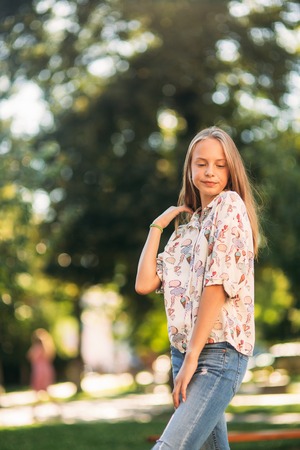 Blonde girl in blouse posing to photographer against the background of green treeの写真素材