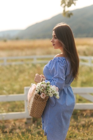 Close up view of beautiful pregnant woman in field holding bouquet and smile. Relax in natureの写真素材