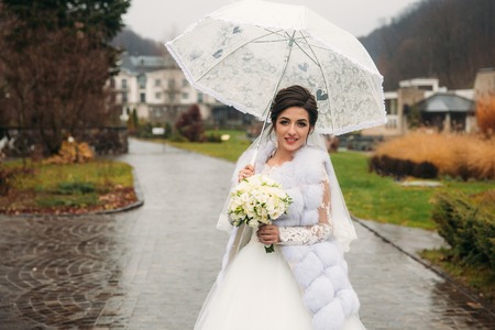 Happy beautiful bride in her weddind day walking in the park. use umbrellaの写真素材