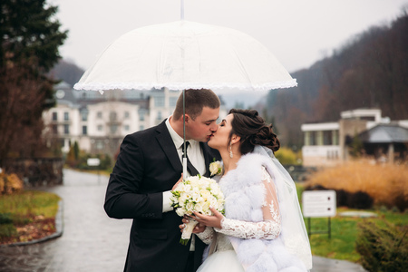 Groom and bride walking in the park on their wedding day. Autumn weather. Rair. Couple umbrellaの写真素材