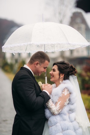 Groom and bride walking in the park on their wedding day. Autumn weather. Rair. Couple umbrellaの写真素材