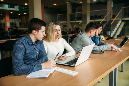 Group of college students studying in the school library, a girl and a boy are using a laptop and...