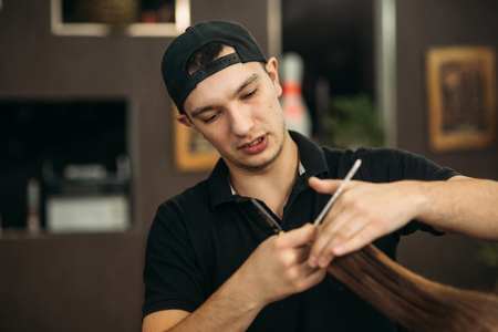 The hands of young barber making haircut to attractive bearded man in barbershopの写真素材