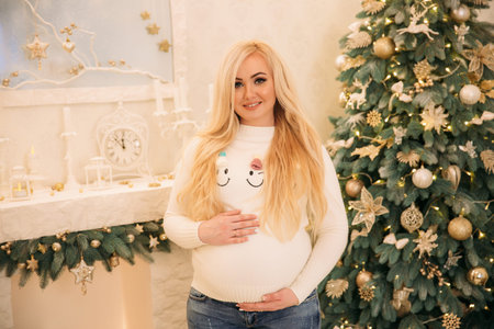 Beautiful pregnant woman puts her hand on her belly. Background of Christmas tree