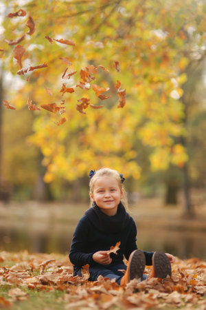 Beautiful young girl sist in leaves and throws them up. Colorful background. Happy little girl smile and have funの写真素材