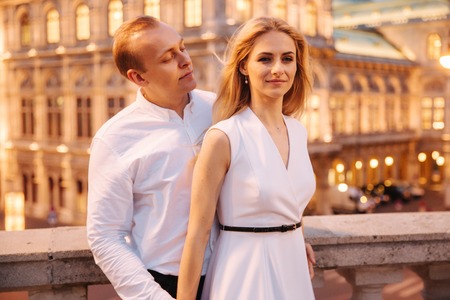 Happy woman and man in white clothes stand by the border in front of city view. City in nightの写真素材