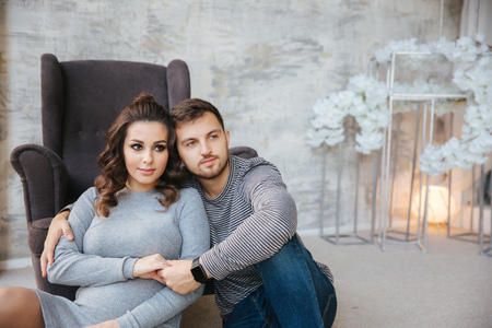 Happy couple sits near the chair in their house. Pregnant woman with her beloved husband. new yearの写真素材