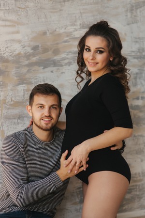 Happy man put his handr on the belly of his pregnant wife. Young family in studio. Couple wait for a babyの写真素材